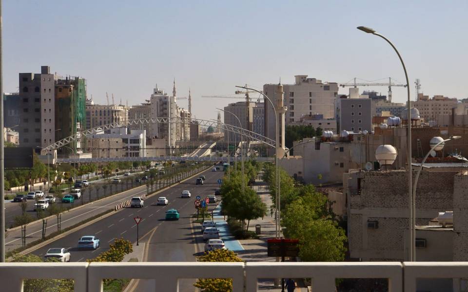 شارع واسع في الرياض تحفه الأشجار وتصطف على جانبيه مبانٍ سكنية وتجارية