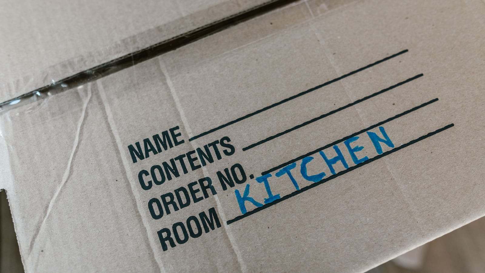 كرتونة نقل مكتوب عليها بخط اليد «KITCHEN» في خانة الغرفة