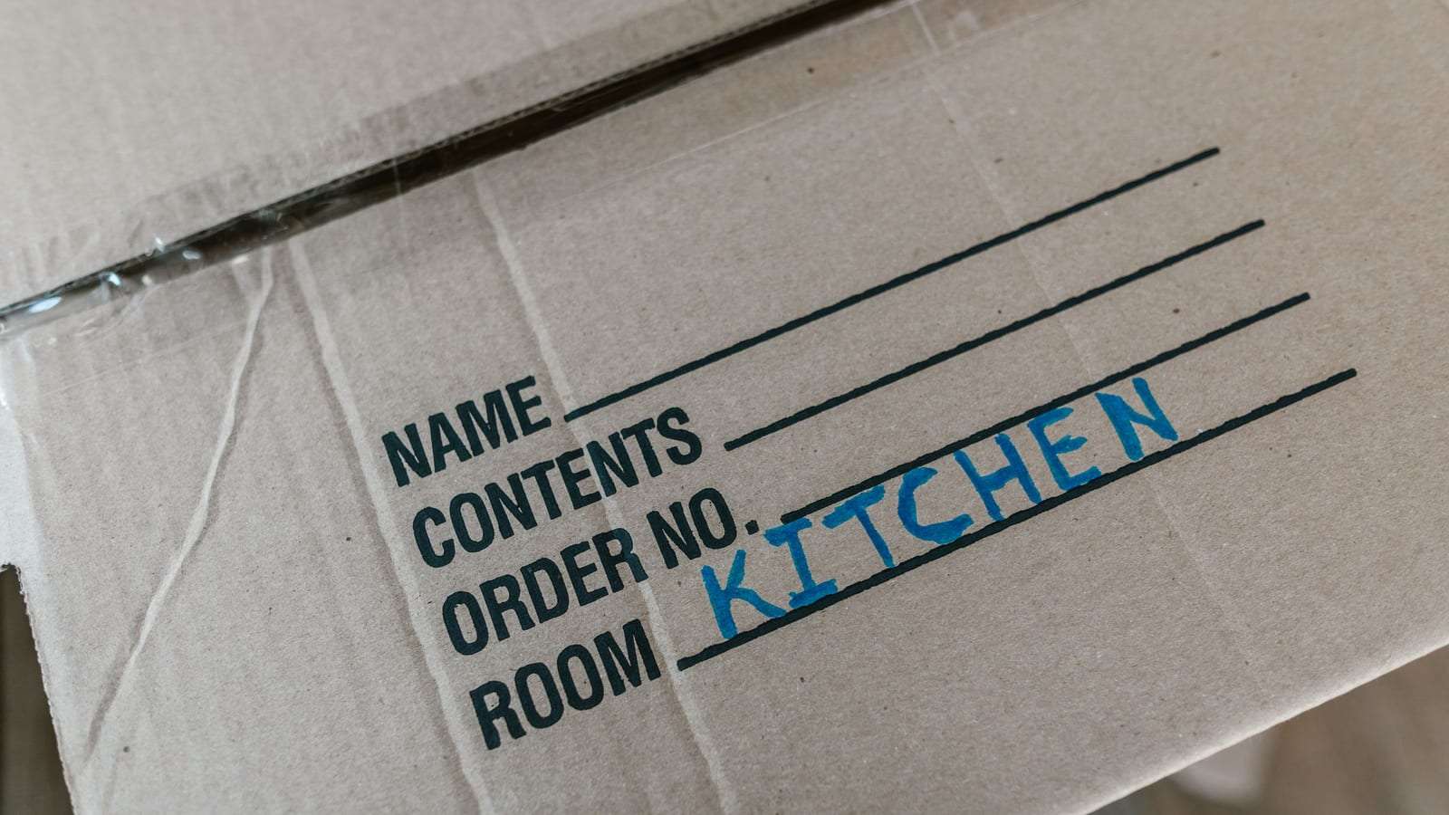 كرتونة نقل مكتوب عليها بخط اليد «KITCHEN» في خانة الغرفة